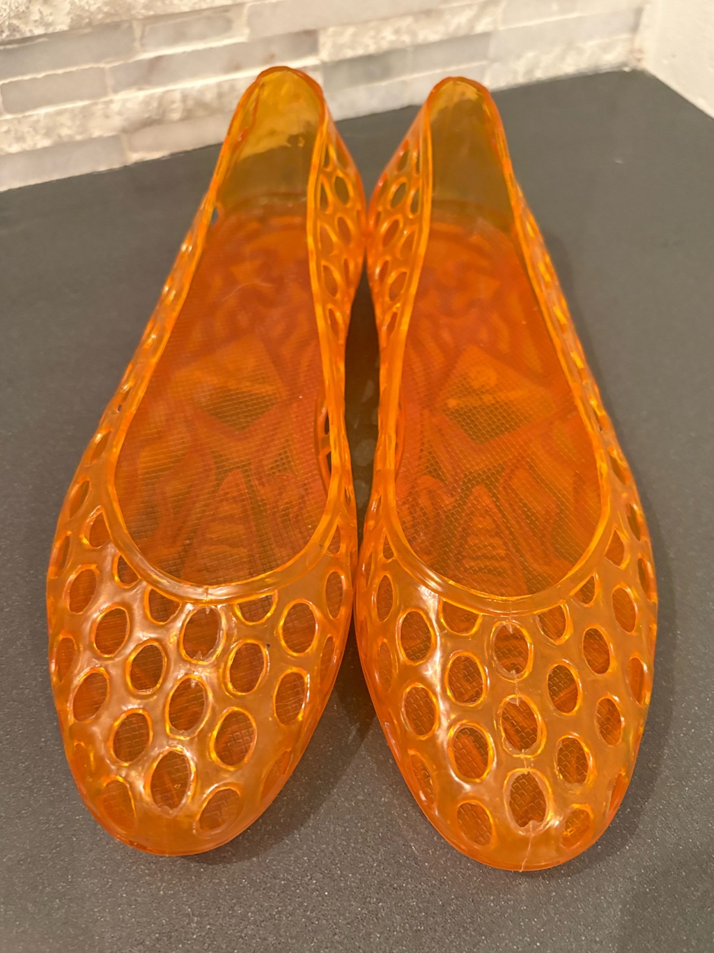 Translucent orange moulded jelly sandals with a cut-out pattern and ankle strap